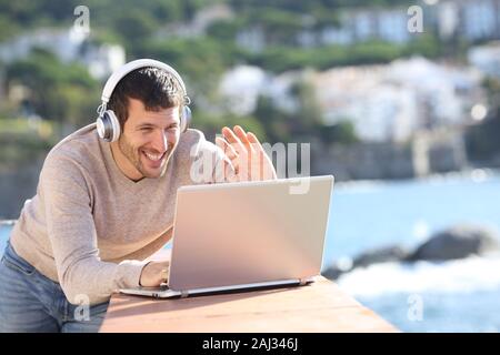 Happy adult man having a video call with a laptop and headphones in a balcony Stock Photo