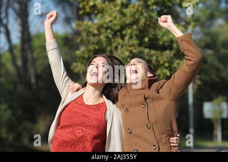 Two excited women celebrating success jumping together in a park in winter