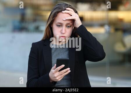 Front view of a frustrated businesswoman reading smart phone content in the street Stock Photo