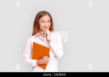 Young businesswoman standing isolated on white background holding notebook posing to camera smiling joyful Stock Photo
