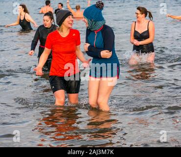 People in the sea for 2020 New Year's Loony Dook or Dip with two young women laughing, North Berwick, East Lothian, Scotland, UK Stock Photo