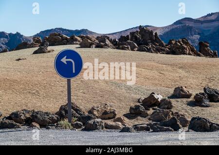 Blue 'Turn left'sign at one of the car parks in Teide National Park in Tenerife, Canary Islands, Spain. Stock Photo
