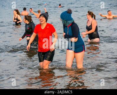 People in the sea for 2020 New Year's Loony Dook or Dip with two young women laughing, North Berwick, East Lothian, Scotland, UK Stock Photo