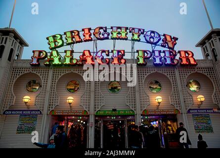 The colourful illuminated sign of Brighton Palace Pier is lit up at dusk. The famous pier at Brighton's seaside of one of the U.K.'s most popular tour Stock Photo