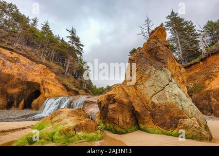 Cloudy skies over sandstone cliffs and waterfall at Hug Point on the Oregon Coast. Stock Photo