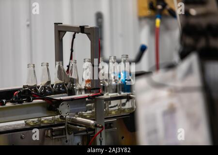 white glass empty beer bottles selective focus, electric pneumatic conveyor belt system machine line, craft brewery factory microbrewery bottling Stock Photo