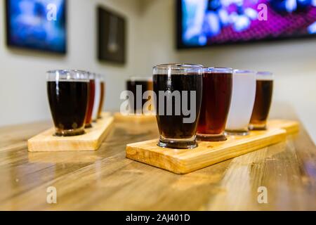 Flight of craft four of different beers glasses on wooden trays during a tasting session, selective focus with blurred bar background and copy space Stock Photo