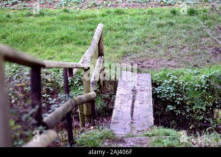 Small wooden foot bridge with railing over ditch in arable field in England Stock Photo