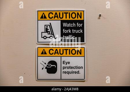two caution signs, watch for fork truck traffic. eye protection required. with symbols, close up with white wall background Stock Photo