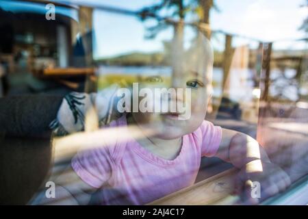 Young toddler girl looks out window with curious expectation. Stock Photo