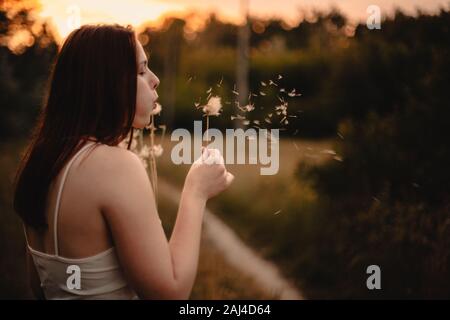 Young woman blowing dandelion while standing on meadow in summer