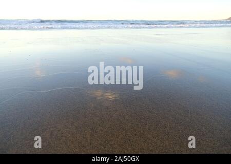 Wave crest on the seashore, clouds and sky reflected in wet surface. Stock Photo