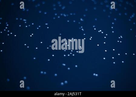 Glowing mica Silver stars confetti on blue color trendy background. Holiday confetti. Classic Flat lay. New Year 2020. Color of the year. Festive holi Stock Photo
