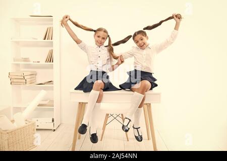 Successful team. Little schoolgirls classmates kids. Schoolgirls friends sit on desk. Best friends relaxing. Schoolgirls tidy hairstyle relaxing havin Stock Photo