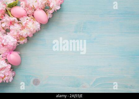 Spring Easter background of painted blue board with branch of flowering cherry covered with pink flowers and pink eggs as a border Stock Photo