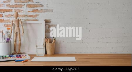 Cropped shot of designer workplace with painting tools and office supplies on wooden table and brick wall background Stock Photo