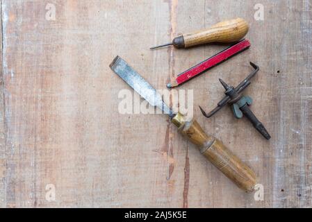 An old chisel and other hand tools lying flat on a rough surface piece of timber with paint marks and scratches Stock Photo