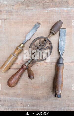 Old chisels and other hand tools lying flat on a rough surface piece of timber with paint marks and scratches Stock Photo