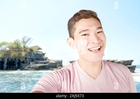 Asian man making selfie using the camera phone with Tanah Lot Temple background Stock Photo
