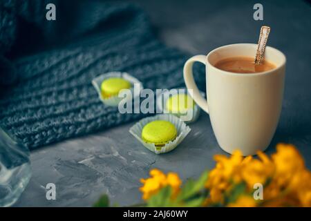 Hot coffee with milk or cream and yellow macaroons on the loft table in a romantic setting with chrysanthemums nearby Stock Photo