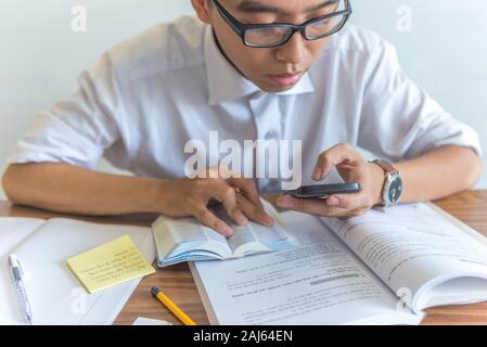Young student using smartphone and doing homework Stock Photo