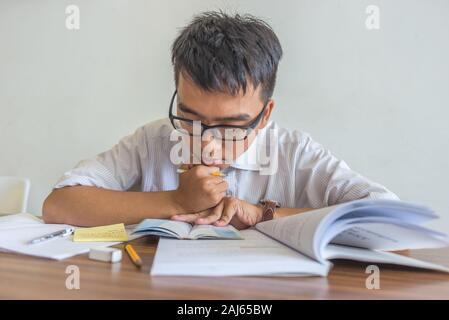 Young Asian student falling asleep while doing homeworks Stock Photo