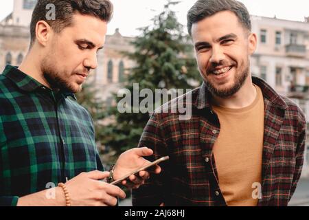 Man using smart phone while his brother standing beside him laughing Stock Photo