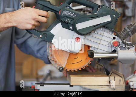 Close-up of young carpenter cutting wooden detail with electric saw in workshop Stock Photo