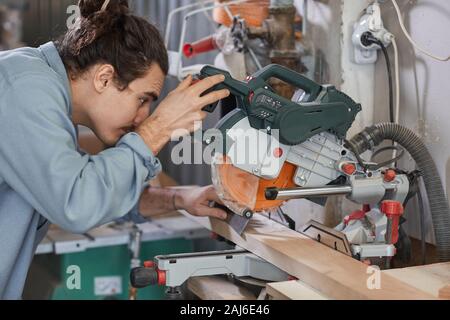 Young man working with electric saw he concentrating on his work and cutting the wooden plank Stock Photo