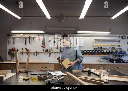 Serious worker making different things from wooden details and using drill in workshop Stock Photo