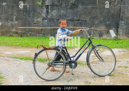 Ho Citadel, Vietnam; May 9 2014. Young boy pushing bicycle and carrying a butterfly-catching net in his mouth. Stock Photo