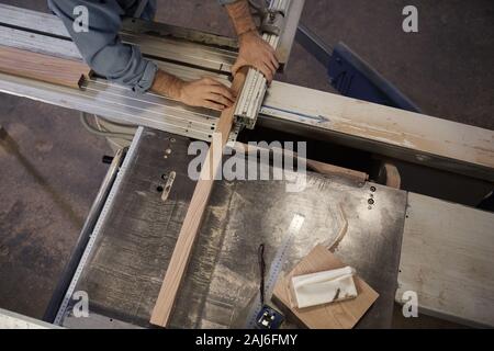 Close-up of young man cutting the wooden plank using lathe during his work in workshop Stock Photo
