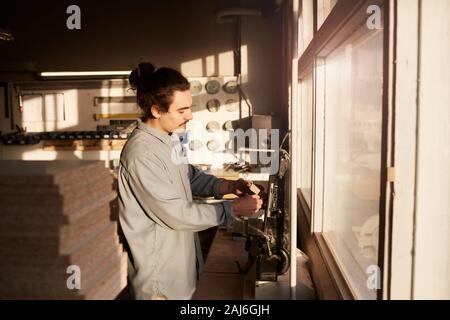 Young manual worker working on carpentry factory he working on lathe and making detail from wood Stock Photo