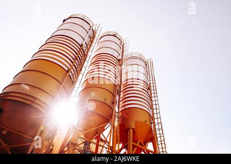 Cement silos of Cement batching plant factory against evening sun flare with warm clear sky Stock Photo