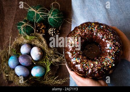 Woman holding chocolate cake with powder next to space galactic Easter eggs in nest next to bump and green filler Stock Photo