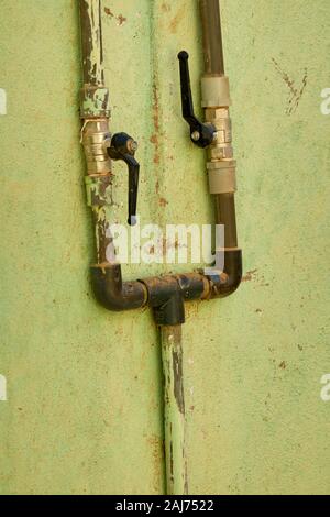 Old water pipes with flaking paint on a green wall in Sudan Stock Photo