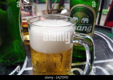 Glass with foamy Chang beer, bottle on background. Chang (Elephant in English) is ThaiBev's flagship brand. Stock Photo
