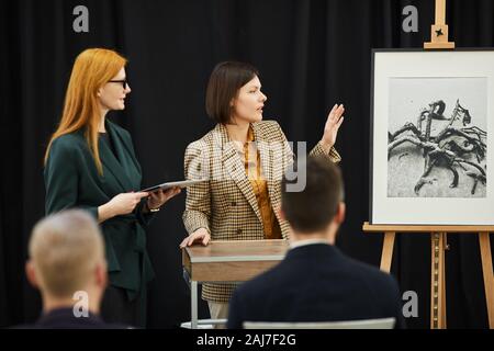 Two businesswomen standing and telling about the painting during conference Stock Photo