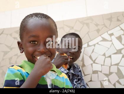 Two bright-eyed Senegalese kids eating snacks during a visit to their village. Senegal, Africa - Photograph: Tony Taylor Stock Photo