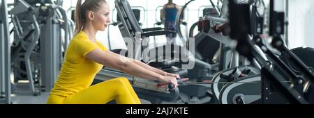 Side view of fit young woman using rowing machine in health club Stock Photo