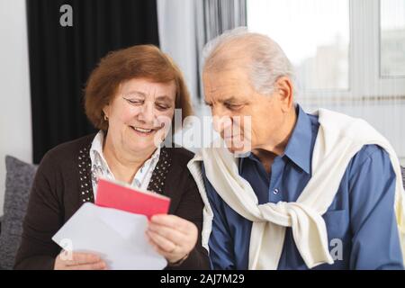 Senior couple standing on the couch and reading a letter received. Portrait Of A Happy Senior Couple At Home Reading Paper Stock Photo