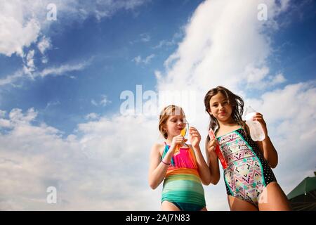 Two Young Girls in Swimsuits With Frozen Treats Against Blue Sky Stock Photo