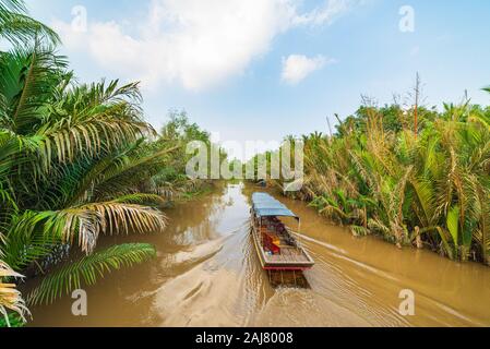 Boat tour in the Mekong River Delta region, Ben Tre, South Vietnam. Wooden boat on cruise in the water channel through coconut palm trees plantation. Stock Photo