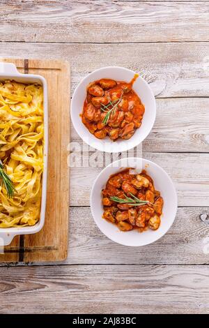 Vertical shot. Baked fettuccine in a ceramic bowl and mussels in tomato sauce on a wooden table. Italian pasta Stock Photo