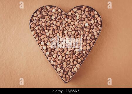 Heap of buckwheat grains on brown background. Heart shaped. Bunch of seeds. Carbohydrate diet concept Stock Photo