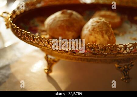 Sweet cookies in a beautiful plate with a golden carved patterned side on sunny table. Stock Photo
