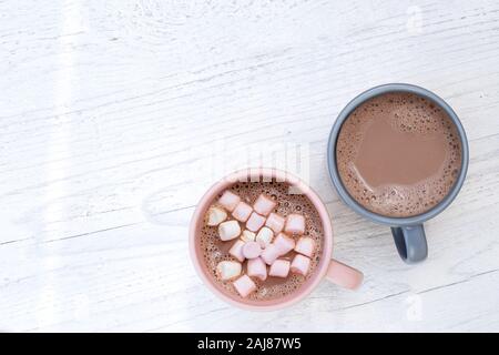 Hot chocolate in two mugs, one with small marshmallows, isolated on white painted wood from above. Space for text. Stock Photo