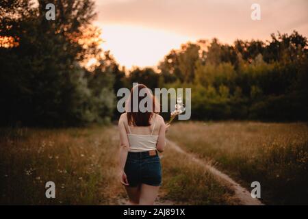 Back view of teenage girl holding bunch of dandelions walking on trail