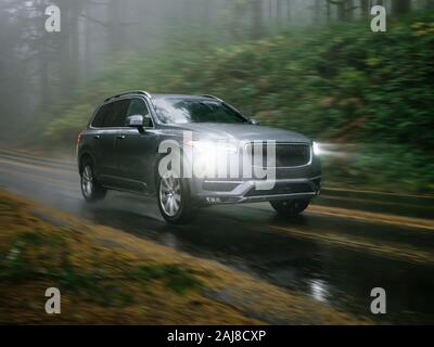 SUV automobile driving through foggy and rainy forest road Stock Photo