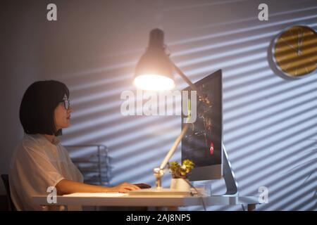 Young designer sitting at her workplace and looking at computer monitor with electric lamp on the table she working late at office Stock Photo